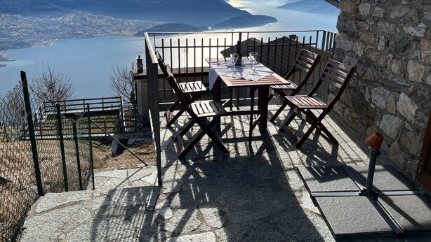 Una terrazza con tavolo e sedie affacciata su un lago e montagne.