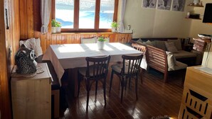 Una stanza accogliente con pareti in legno e un'ampia finestra, un tavolo da pranzo con sedie, un divano e un armadietto in legno.