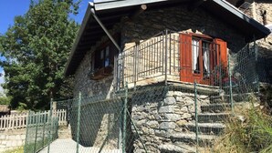 Una casa in pietra con un balcone in legno, una scala in pietra e una recinzione in rete metallica.