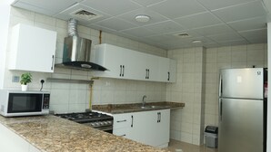A modern kitchen with white cabinets, a stainless steel stove, a microwave, and a refrigerator. - Hawana Premium Hostel (Dubai)