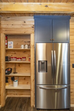 A stainless steel refrigerator with a freezer compartment, built into a wooden wall with shelves above.