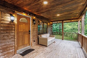 A wooden cabin with a porch, a door with a glass panel, and a wicker sofa.