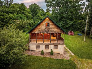 A log cabin with a porch, a small shed, and a well-maintained lawn.