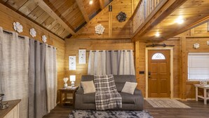 Interior acogedor de una cabaña de madera con un sofá gris, una manta escocesa y una alfombra mullida.