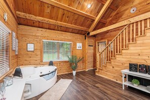 A wooden cabin interior with a hot tub, a staircase, and a potted plant.