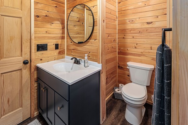 Une salle de bain avec des murs recouverts de panneaux en bois, un lavabo blanc avec un robinet noir, des toilettes et un miroir.