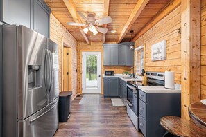 A modern kitchen with wooden walls, a stainless steel refrigerator, and a ceiling fan.