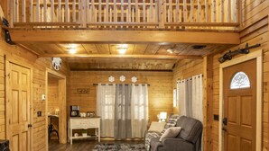 Interior de una cabaña de madera con balcón, sofá, escritorio y chimenea.