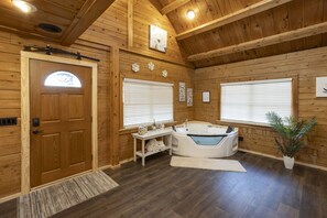 A wooden cabin interior with a wooden door, a large bathtub, and a small table with towels.
