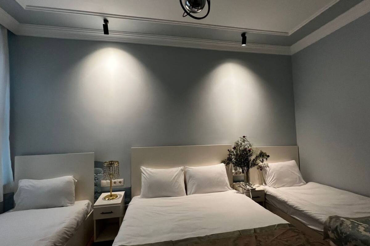A hotel room with two single beds, a nightstand with a lamp, a vase with flowers, and a ceiling light fixture.
