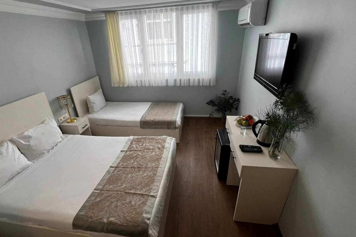 A hotel room with two beds, a TV, a desk with a plant, and a window with curtains.
