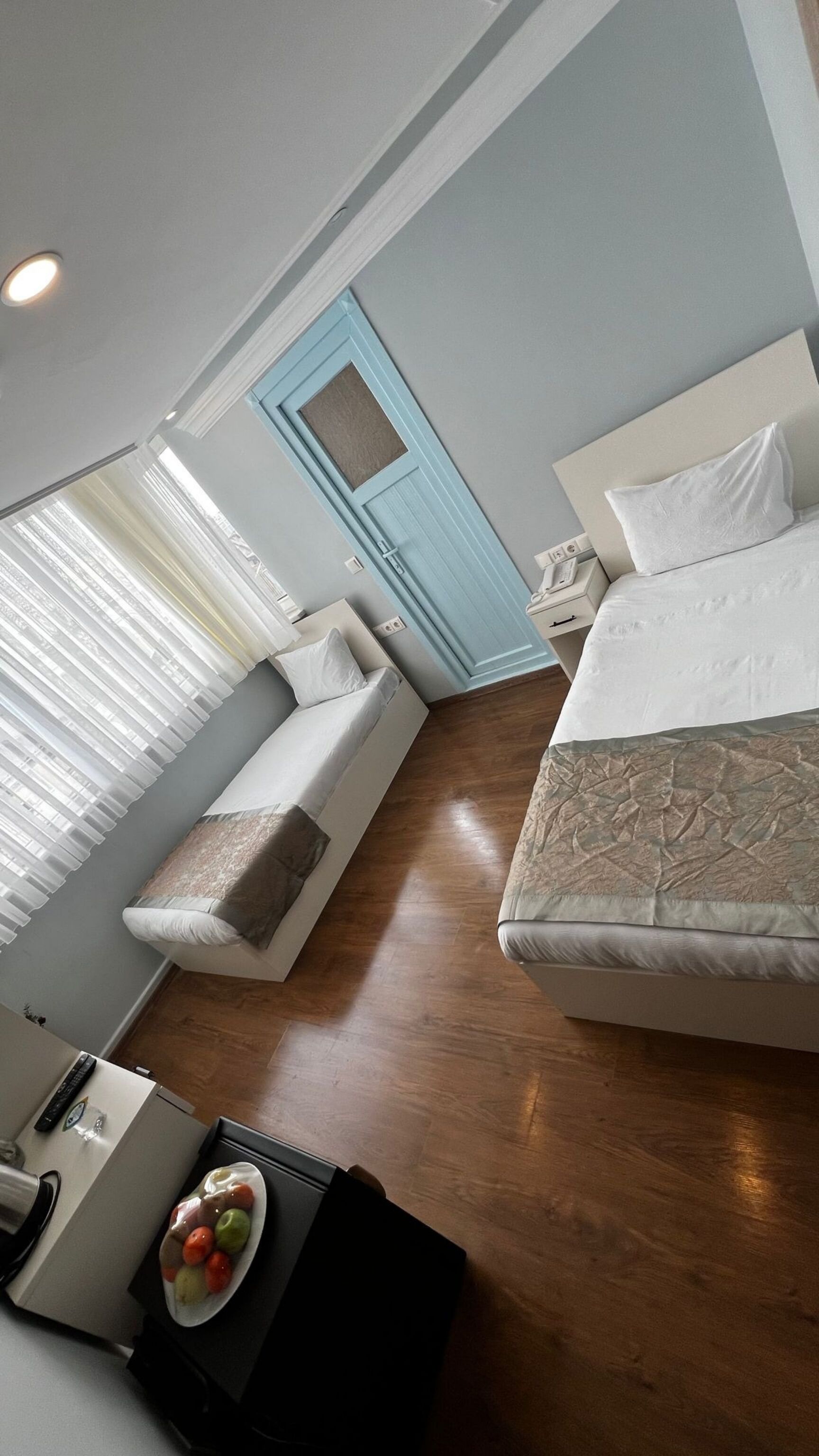 A modern hotel room with a bed, a sofa, a desk, and a small table with fruit.