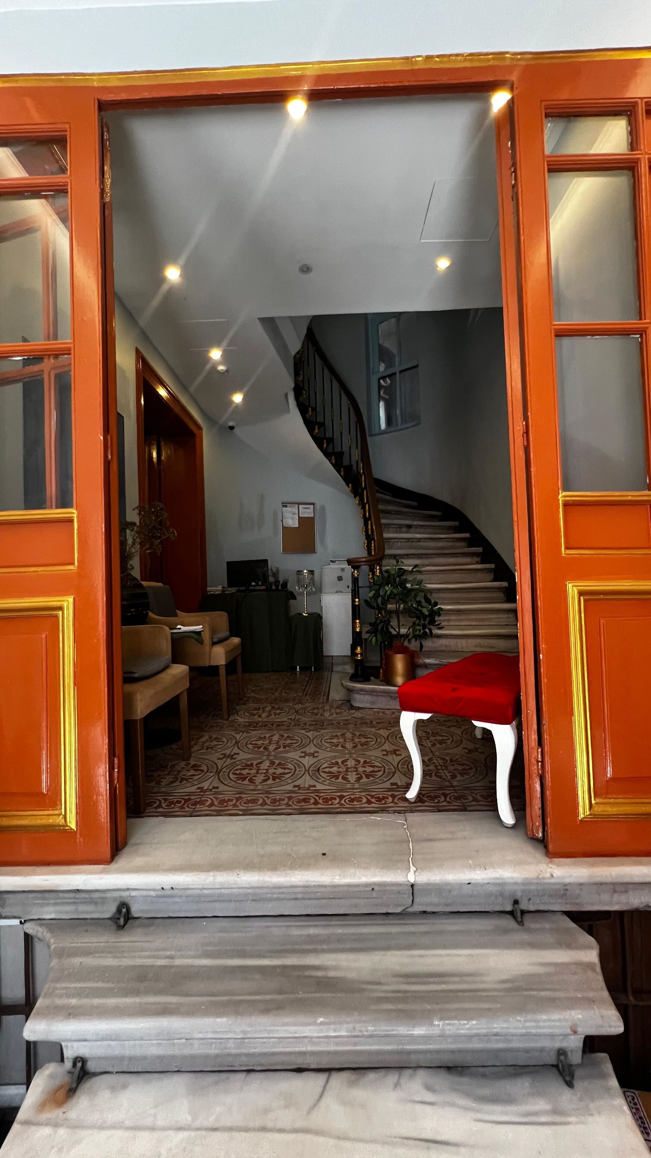 A grand staircase leading to a second floor, a cozy seating area with a red sofa, and a small table with a vase.