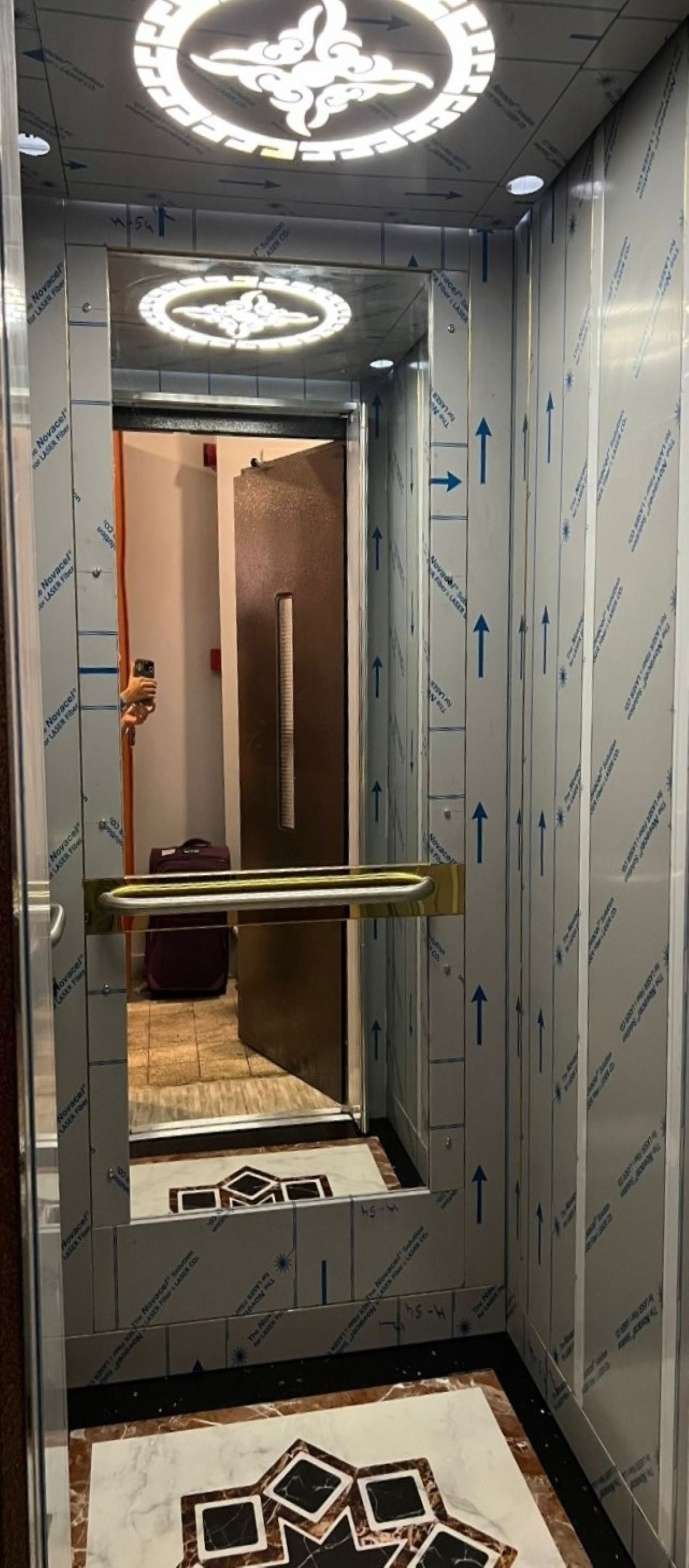An elevator with directional arrows on the walls, a handrail, and a patterned floor.