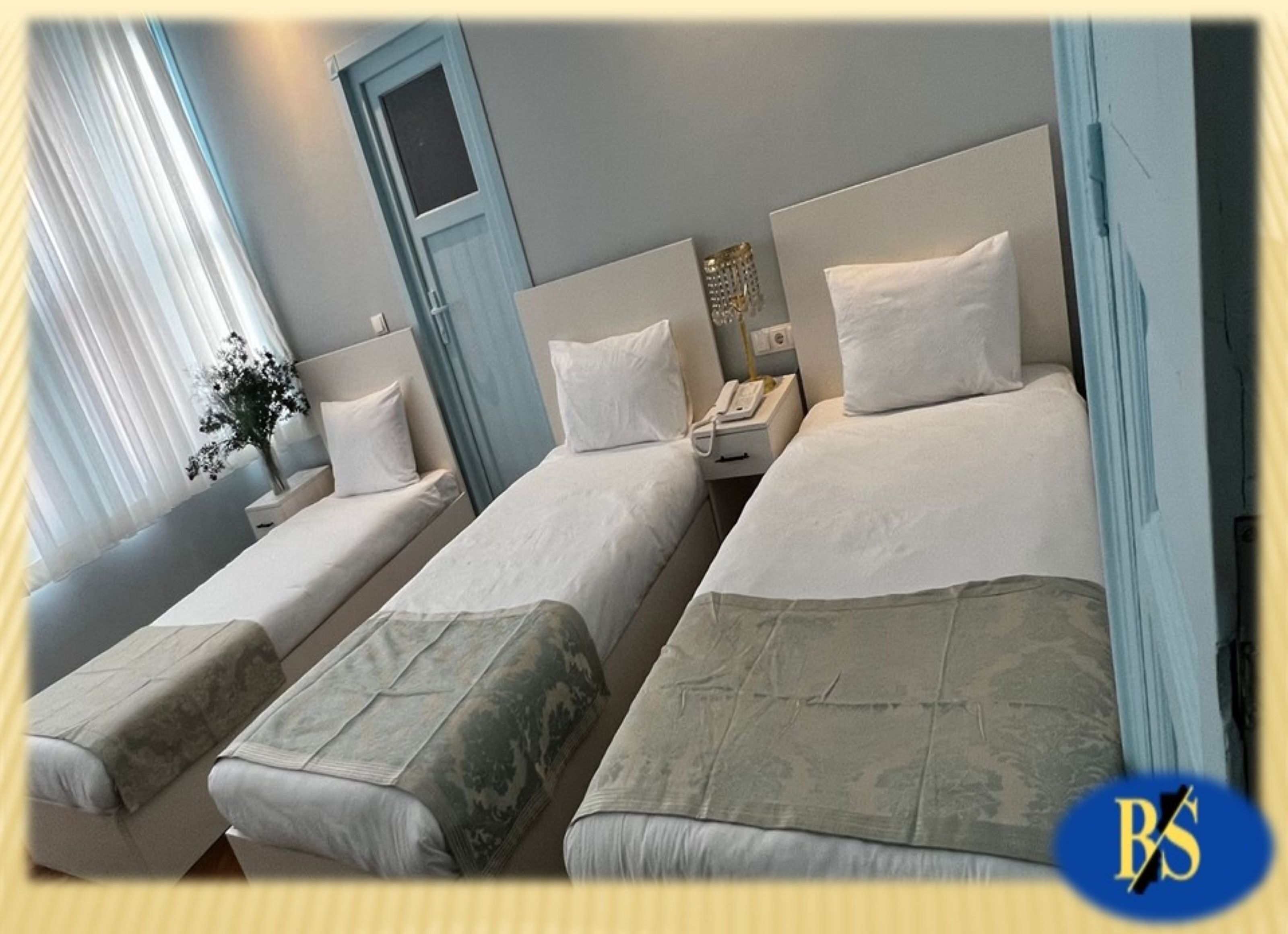 Une chambre d’hôtel avec deux lits simples, une table de chevet avec un téléphone et une fenêtre avec des rideaux.