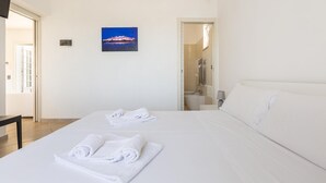 Ett hotellrum med två sängar, vita sängkläder, en målning som föreställer ett landskap, ett badrum som syns genom en öppen dörr och en platt-TV som är monterad på väggen.