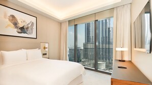 A modern hotel room with a large bed, a city view, a bedside table with a lamp, and a framed artwork on the wall. - Luxury StayCation - Modern Comfort: 3-BR at The Address Opera (Dubai)