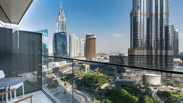 A high-rise building with a modern glass facade, a curved glass balcony, and a view of a cityscape with various skyscrapers. - Luxury StayCation - Modern Comfort: 3-BR at The Address Opera (Dubai)
