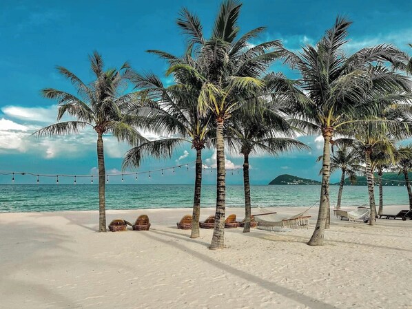 A beach with palm trees, string lights, and beach huts. - Pearl Vista Boutique Hotel (Phu Quoc)