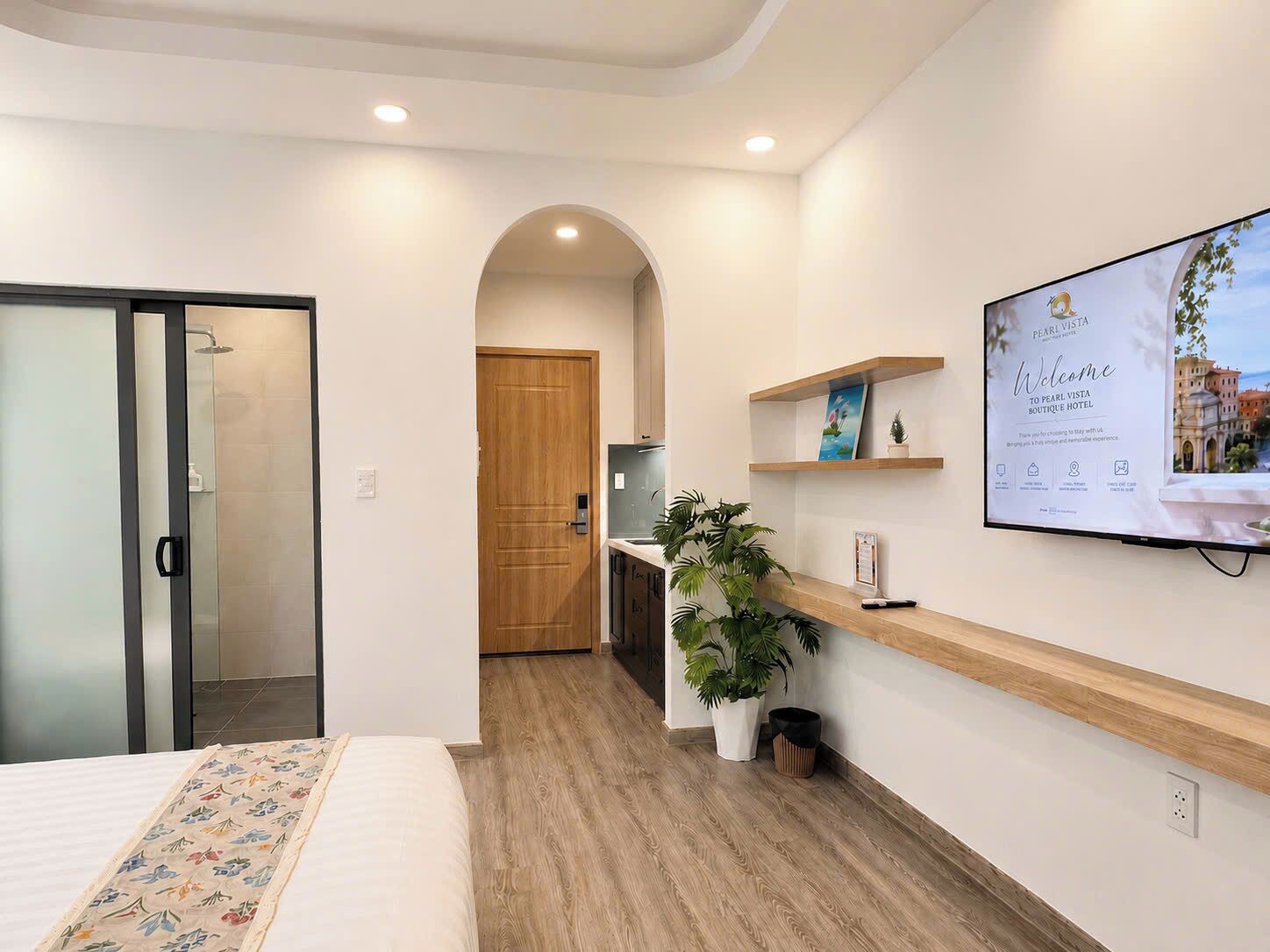 Une chambre d’hôtel avec un lit, un bureau, une plante et un téléviseur fixé au mur qui affiche un message de bienvenue.