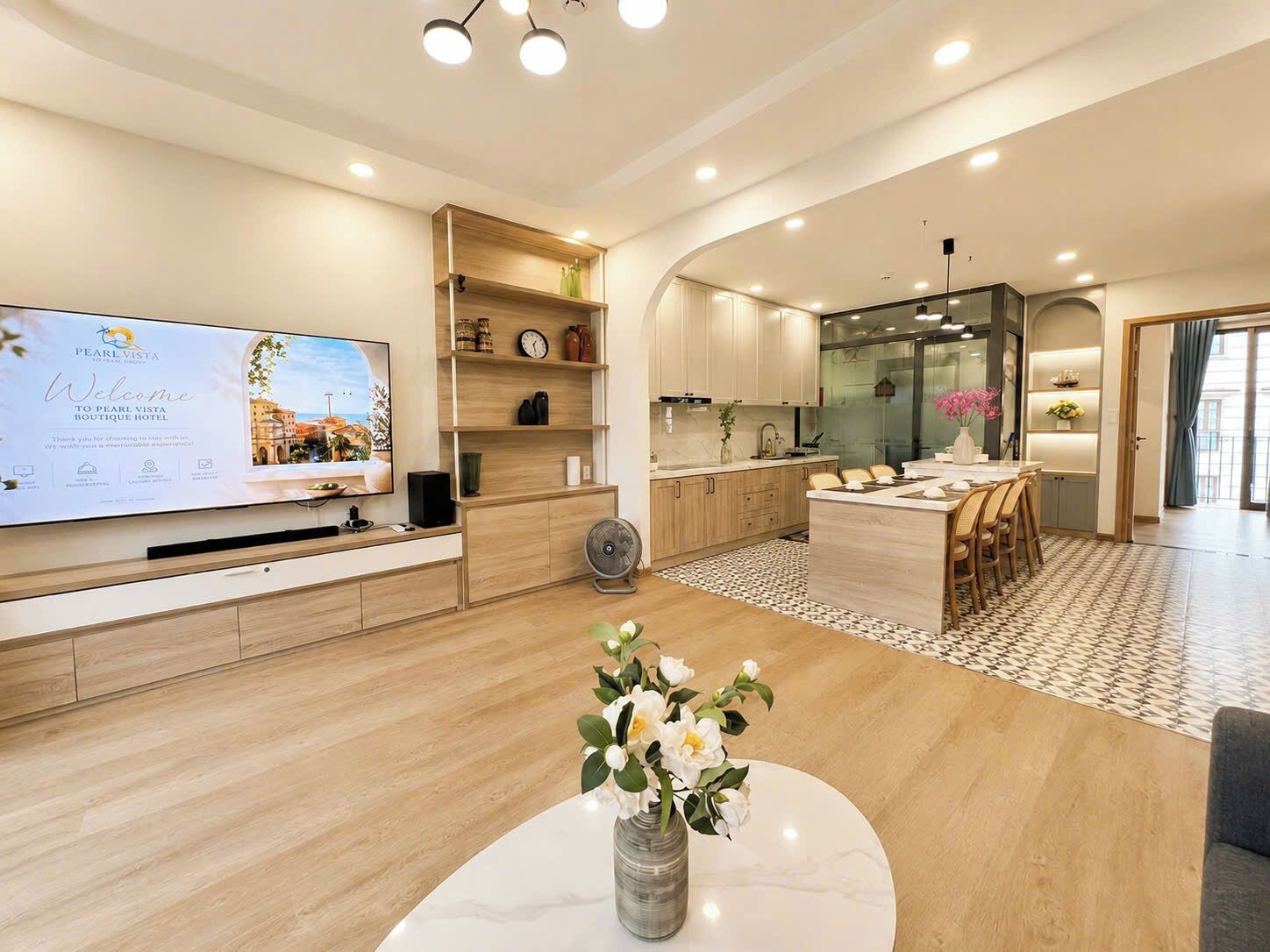 Una habitación de hotel moderna con televisión de pantalla plana, muebles de madera, un comedor con una isla central y un ventanal grande.