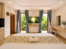 Un dormitorio con cama, televisión, escritorio y balcón con cortinas.