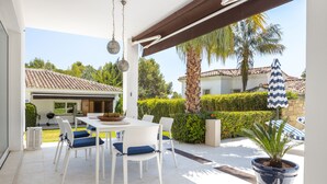 An outdoor patio with a white table and chairs, a potted plant, and a blue and white striped umbrella. - Buccara Casa Bruno (Marbella)