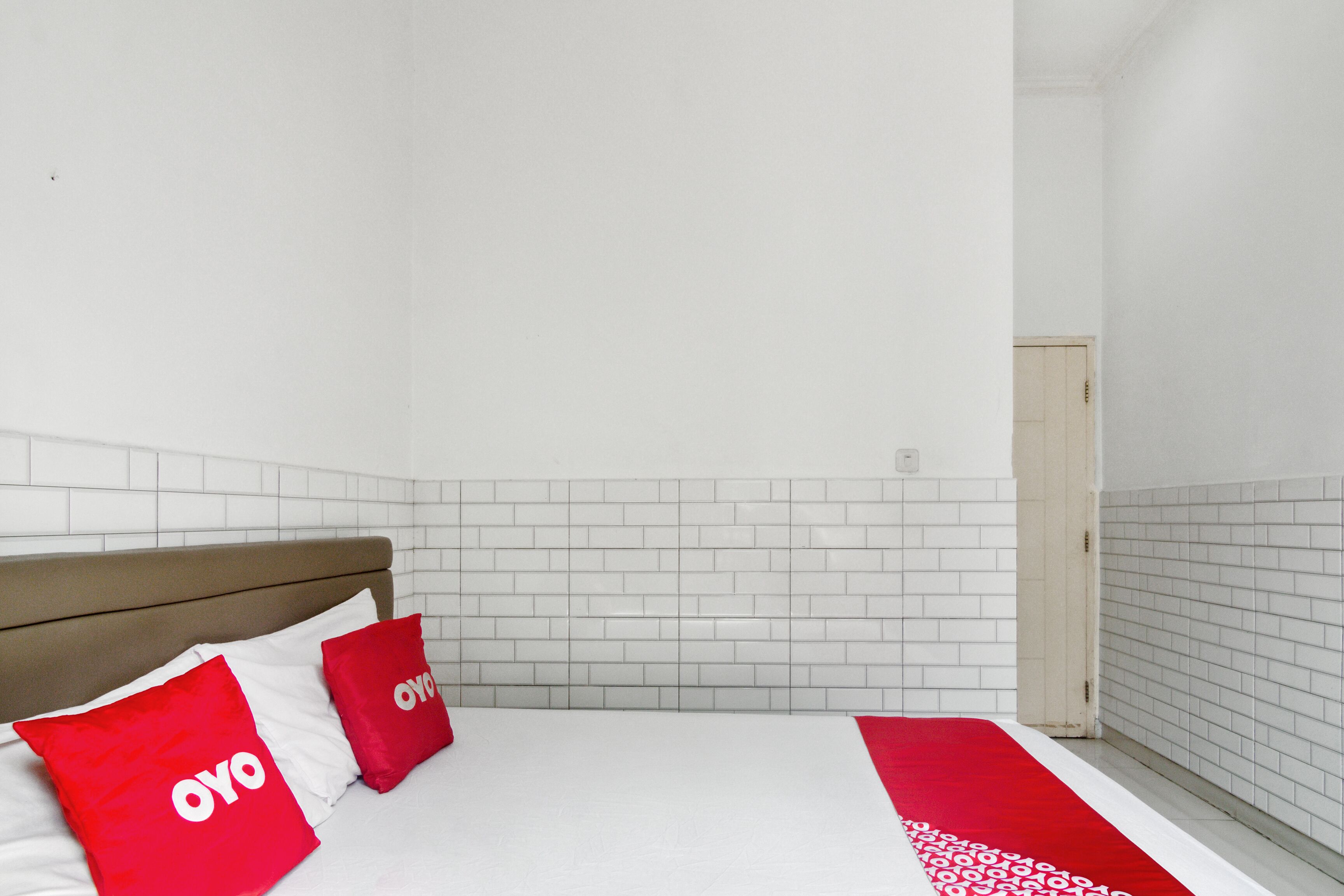 A hotel room with a bed, white tiled walls, and a wooden headboard.