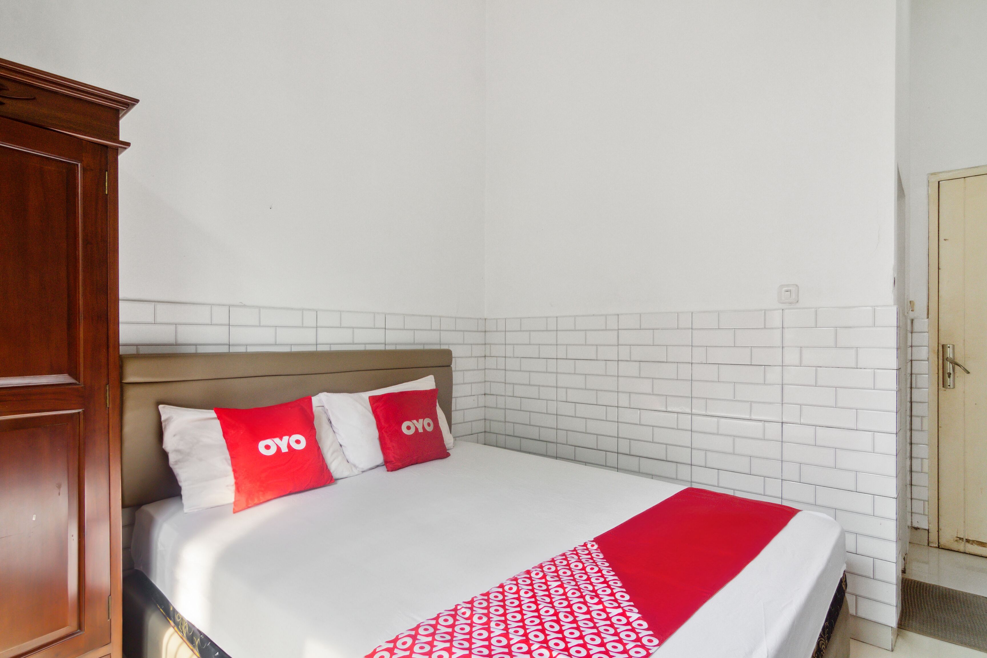 A hotel room with a bed, white tiled walls, and a wooden wardrobe.