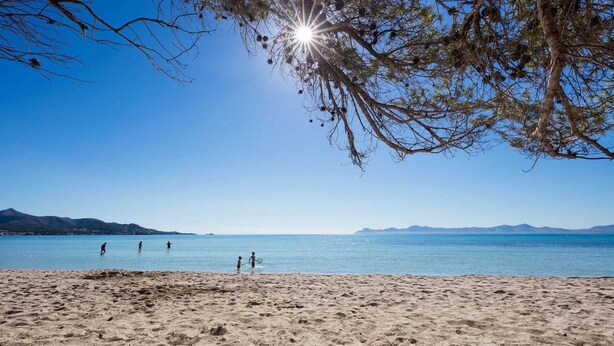 A beach with clear skies, calm water, and distant mountains.