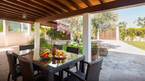 An outdoor patio with a glass table, wicker chairs, and a fruit bowl.