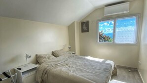 Un dormitorio con cama, mesitas de noche, un escritorio y un equipo de aire acondicionado.