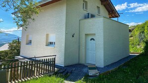 Una casa de dos pisos con fachada blanca, techo de madera y un pequeño porche delantero.