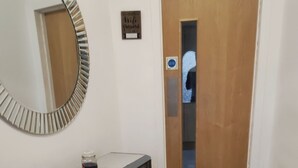 Een hal met een houten deur, een console tafel met een klein reservoir, en een kamerbreed tapijt op de vloer.