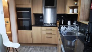 Een kleine keuken met houten kastjes, een ingebouwde oven, een magnetron en een roestvrijstalen spoelbak.
