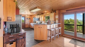 A wooden cabin with a kitchen featuring a central island, bar stools, and a view through the glass door. - Pet + Family Friendly, 4 mins to Golf, on the Bourbon Trail, & close to the Ark! (Owenton)