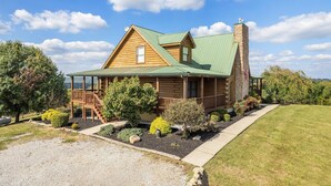 A log cabin with a green roof, a stone chimney, and a deck with stairs leading to a porch. - Pet + Family Friendly, 4 mins to Golf, on the Bourbon Trail, & close to the Ark! (Owenton)