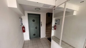 Um corredor com piso de azulejos, uma porta verde e um extintor de incêndio à esquerda.