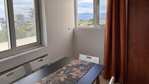 Quarto com uma mesa de jantar, duas cadeiras, janela com vista para edifícios e montanhas, e cortina marrom.