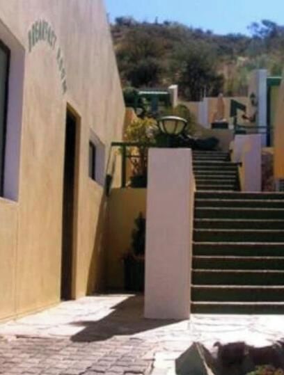 A hotel entrance with a staircase leading to the main building, surrounded by a garden with flowers.