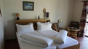Quarto de hotel com uma cama grande, cabeceira de madeira, uma mesa pequena, uma cadeira e um quadro na parede.