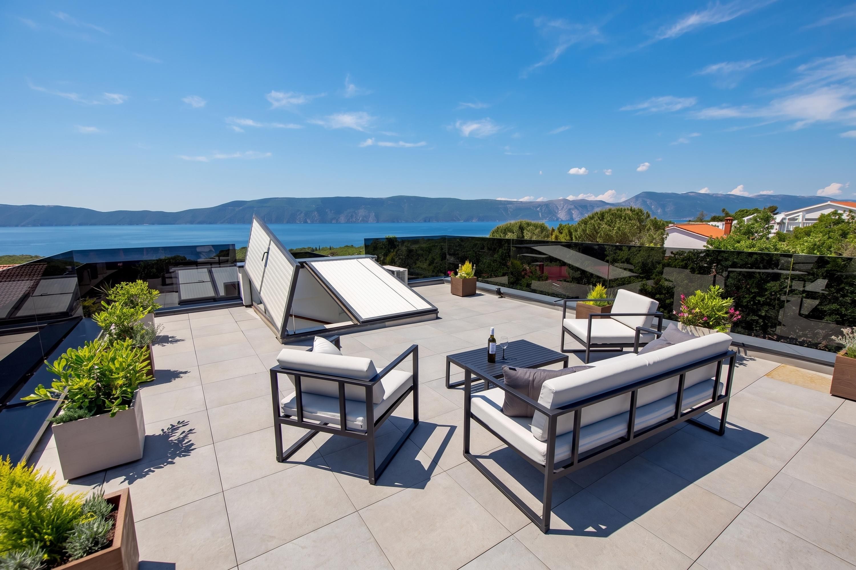Terraço ao ar livre com assentos, vista para o mar e montanhas ao longe.