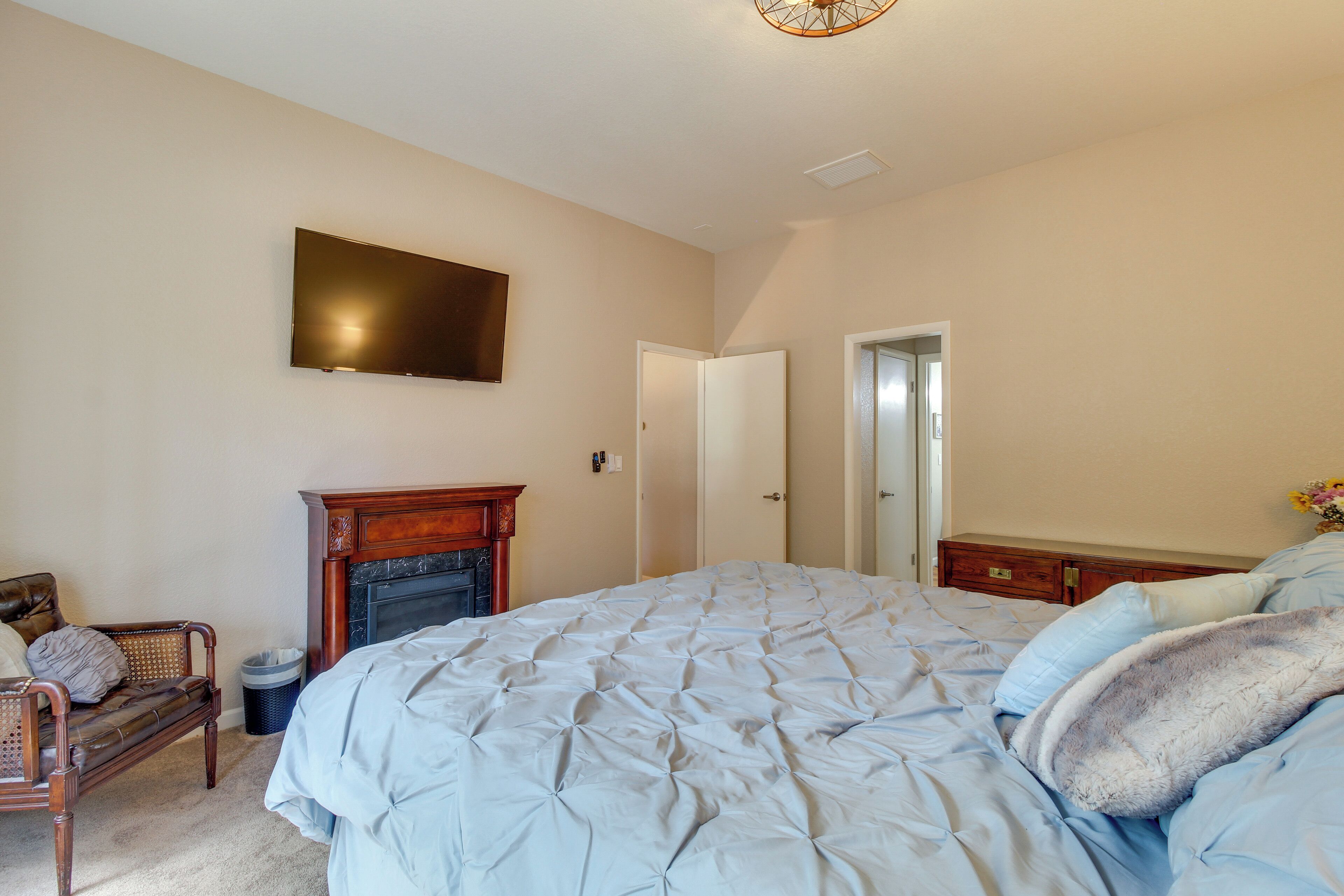 A bedroom with a large bed, a fireplace, a television mounted on the wall, and a door leading to another room.