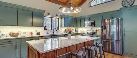 A spacious kitchen with a large island, wooden bar stools, and a stainless steel refrigerator.