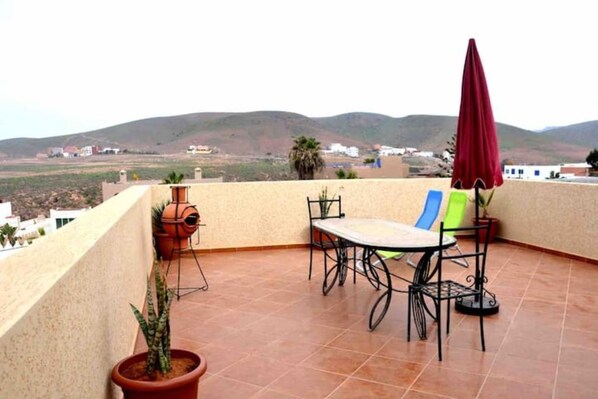 A terrace with a table and chairs, a red umbrella, and potted plants.