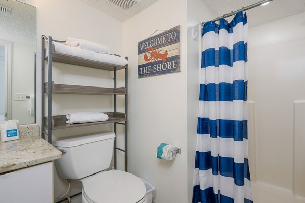 A bathroom with a bunk bed, a toilet, a shower curtain, and a welcome sign.