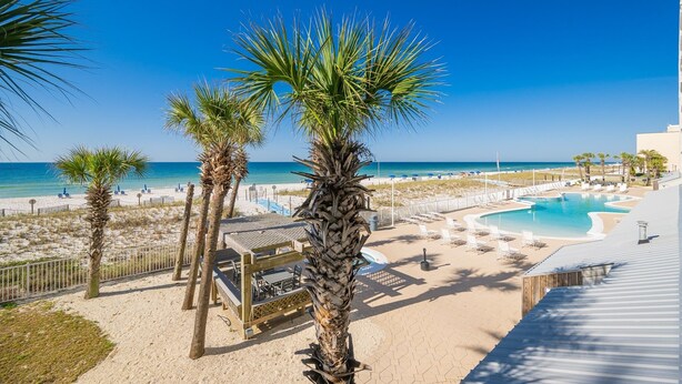 A beachside resort with a pool, palm trees, and a view of the ocean. - Ocean House 2202 2 Bedroom Condo (Gulf Shores)