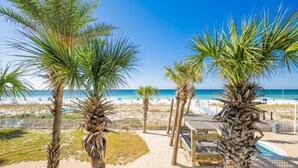 A beach view with palm trees, a pool, and a beach area with umbrellas. - Ocean House 2202 2 Bedroom Condo (Gulf Shores)
