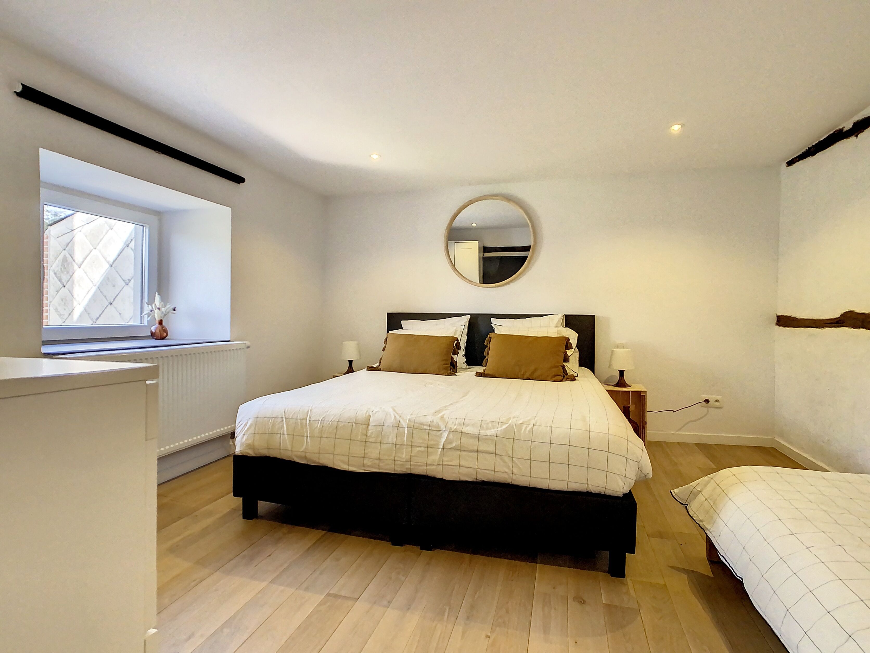 A bedroom with a large bed, a smaller bed, a window, a mirror, and a radiator.