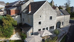 Un bâtiment en pierre avec un toit en pente, un petit jardin agrémenté d’une table et de chaises, et une allée pavée.
